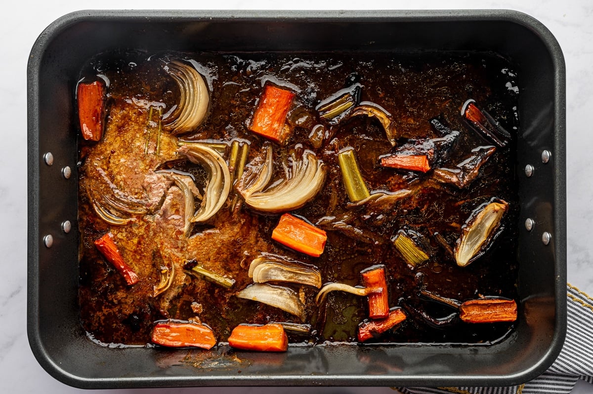 Roasted vegetables and rich turkey drippings in pan before straining.