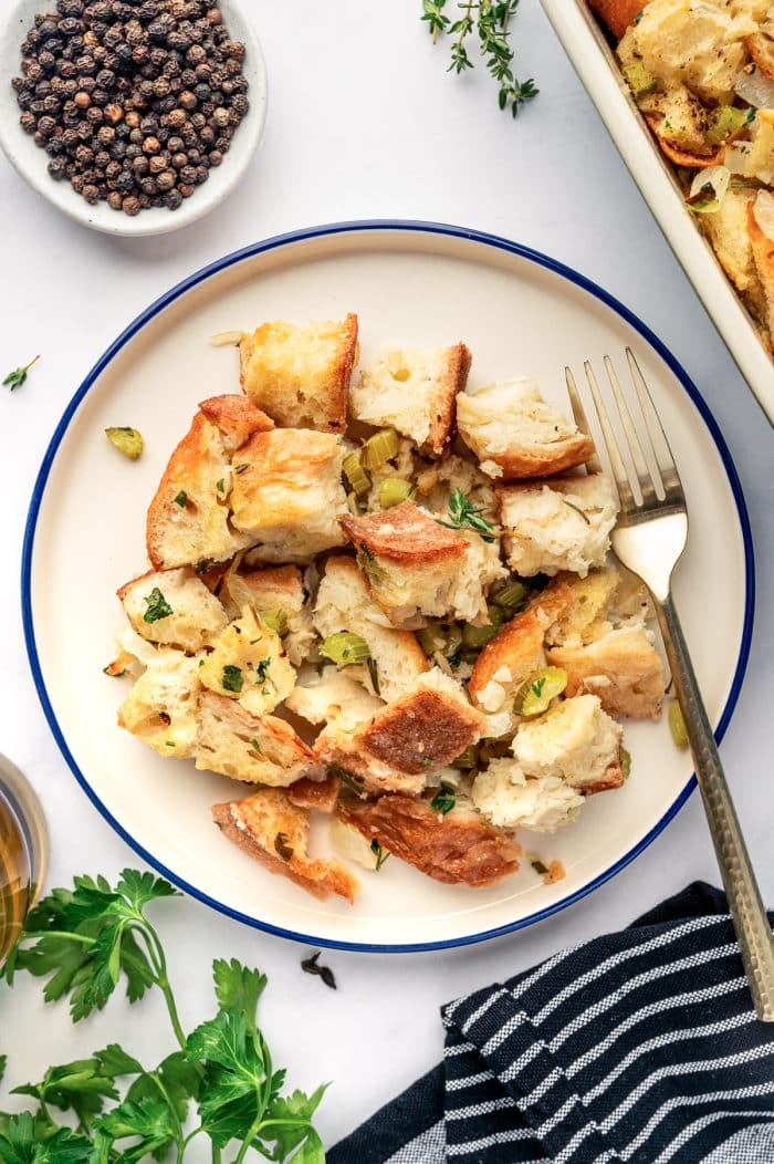 Serving of homemade Thanksgiving dressing on a white plate with a fork, garnished with fresh herbs.