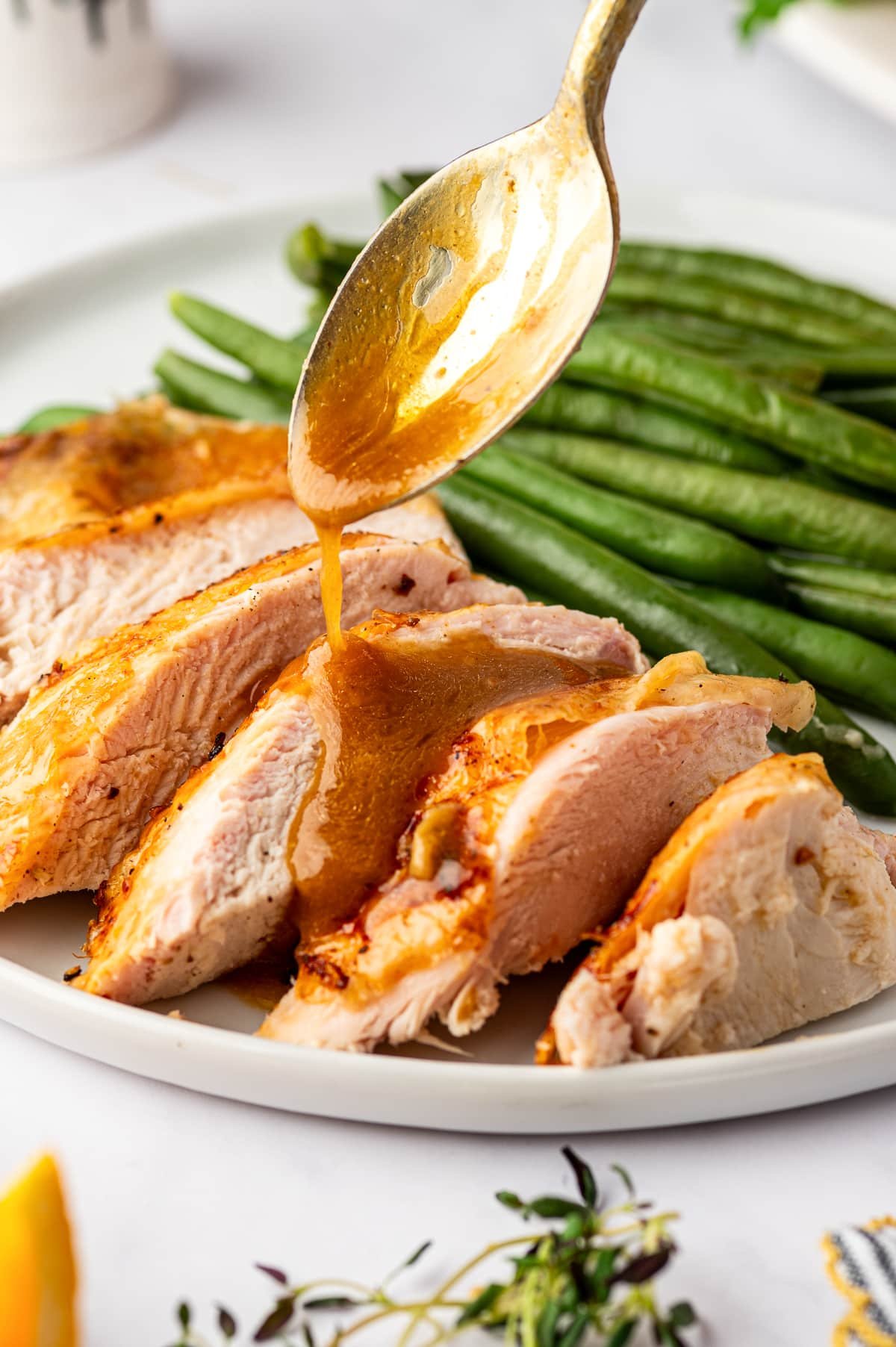 A spoon pouring warm turkey gravy over juicy slices of roasted turkey breast for a Thanksgiving meal.