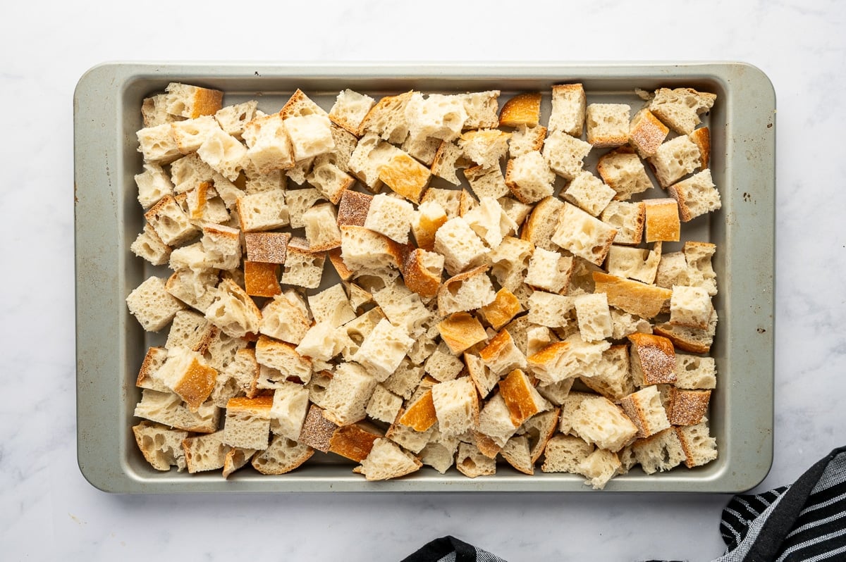 Cubed sourdough bread spread evenly on a baking sheet to dry for homemade Thanksgiving dressing.