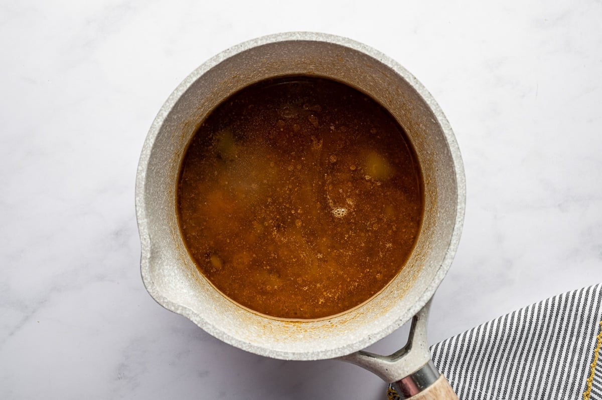 Brown gravy made from turkey drippings simmering in a saucepan as it thickens into a silky sauce.