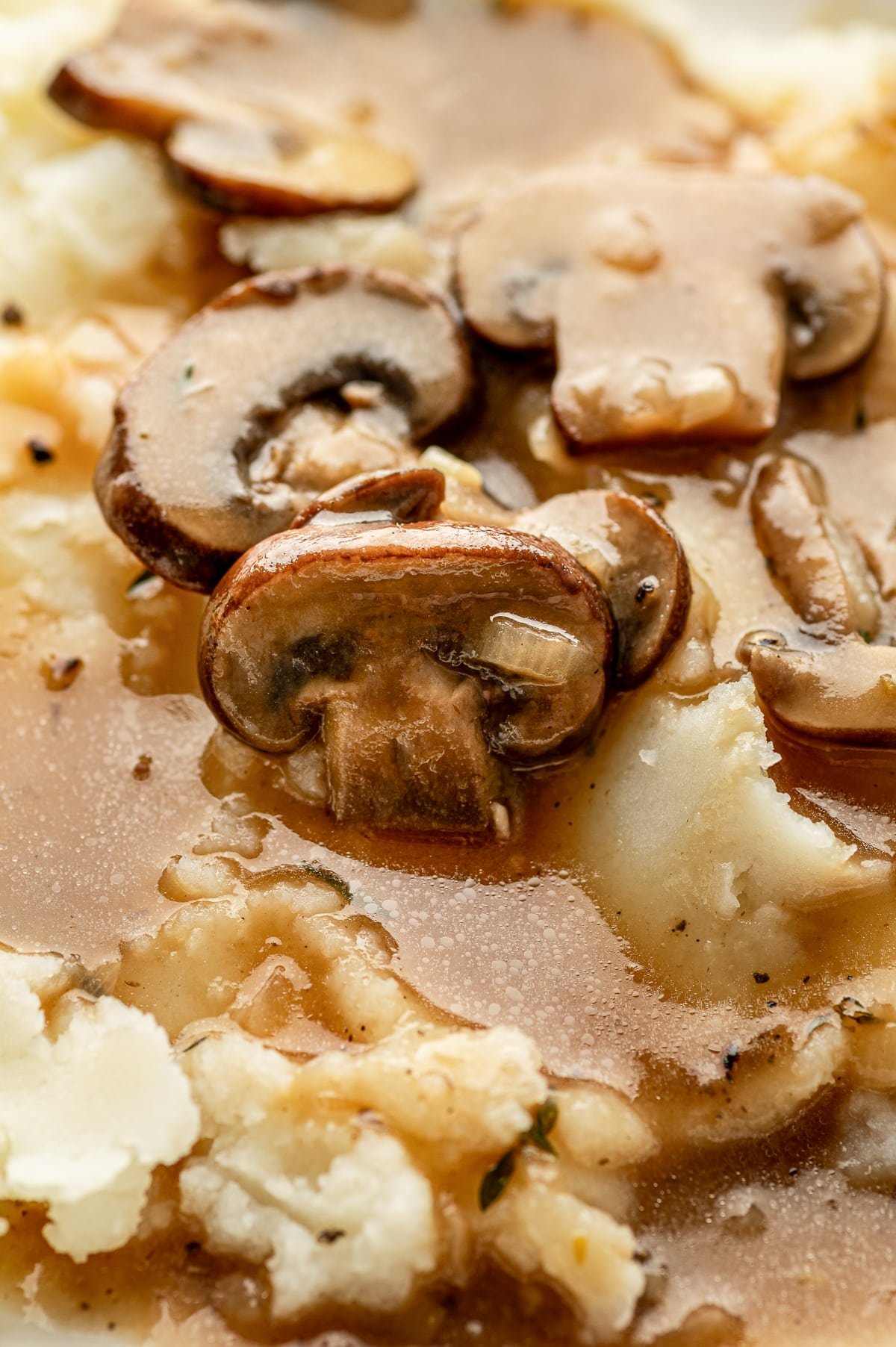 Extreme close-up of mushroom slices coated in gravy over mashed potatoes.