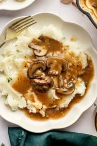 Closer view of mashed potatoes smothered in mushroom gravy on a scalloped plate.