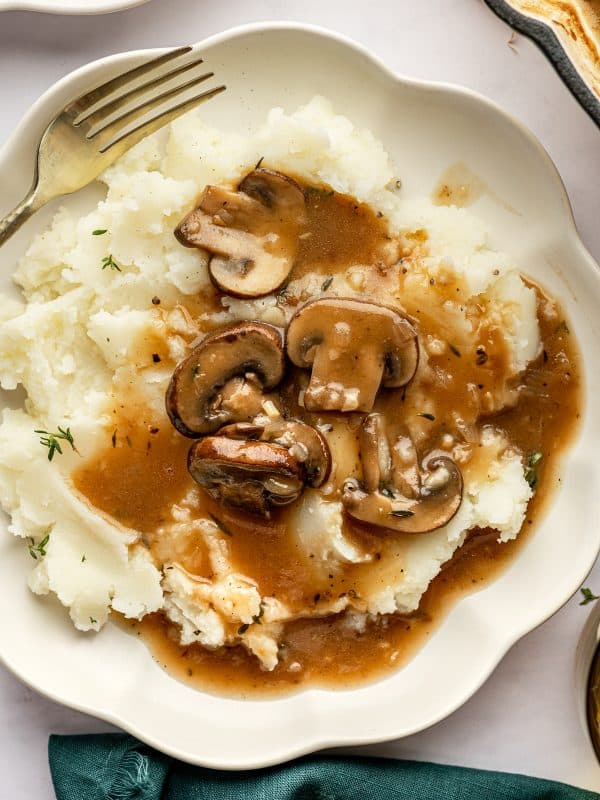 Closer view of mashed potatoes smothered in mushroom gravy on a scalloped plate.