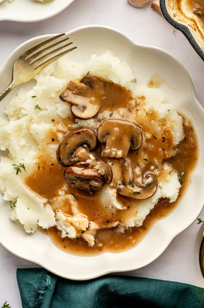 Closer view of mashed potatoes smothered in mushroom gravy on a scalloped plate.