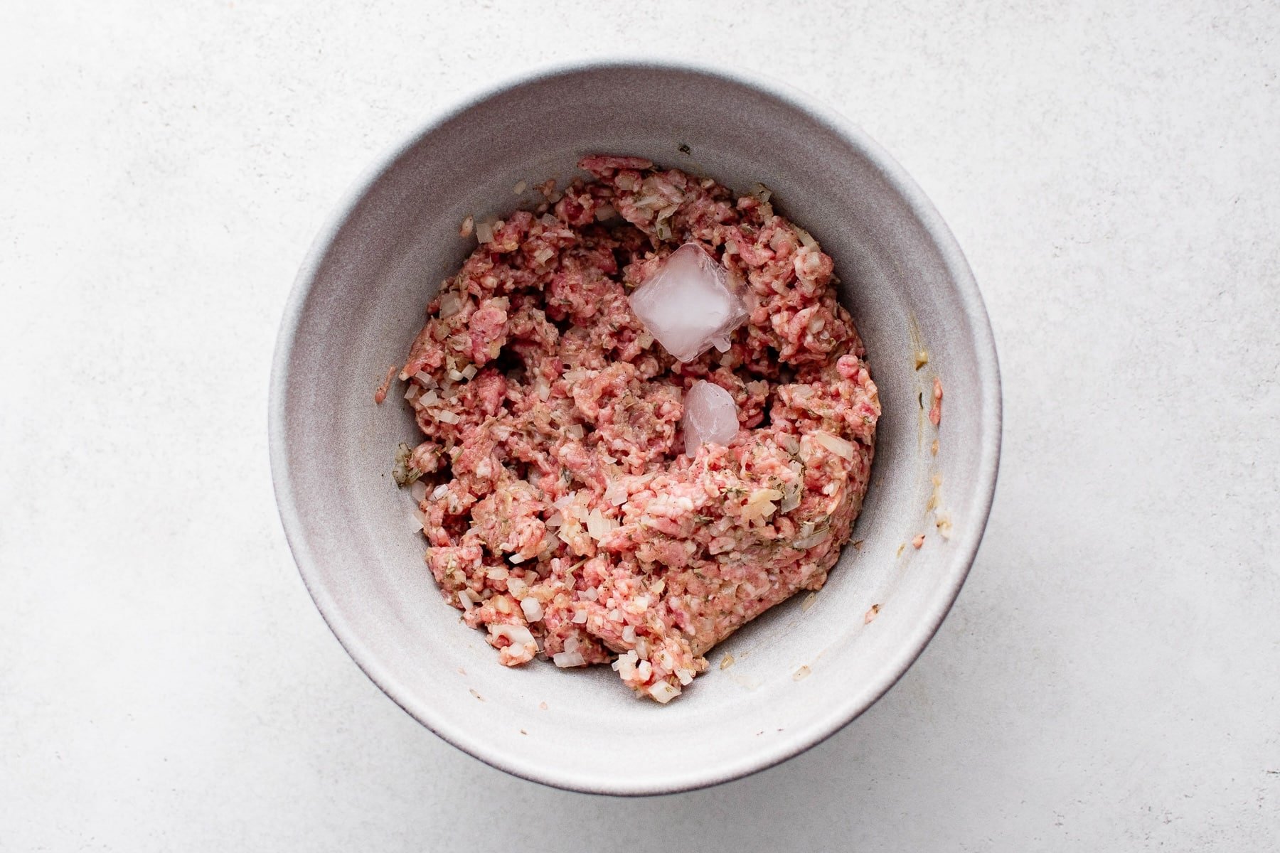 Mixed sausage roll filling in a bowl with a few ice cubes on top.