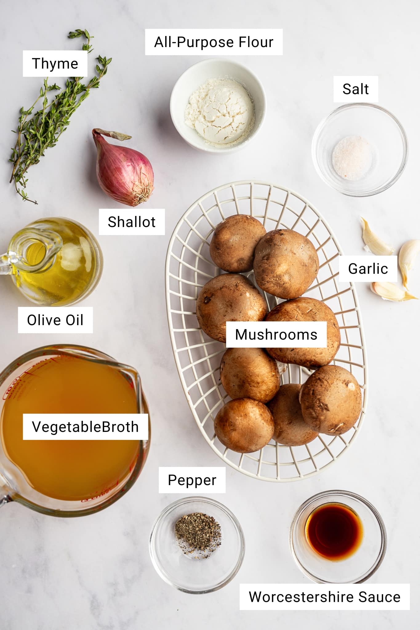 Overhead view of ingredients for mushroom gravy including mushrooms, broth, shallot, garlic, thyme, flour, olive oil, salt, pepper, and Worcestershire sauce.