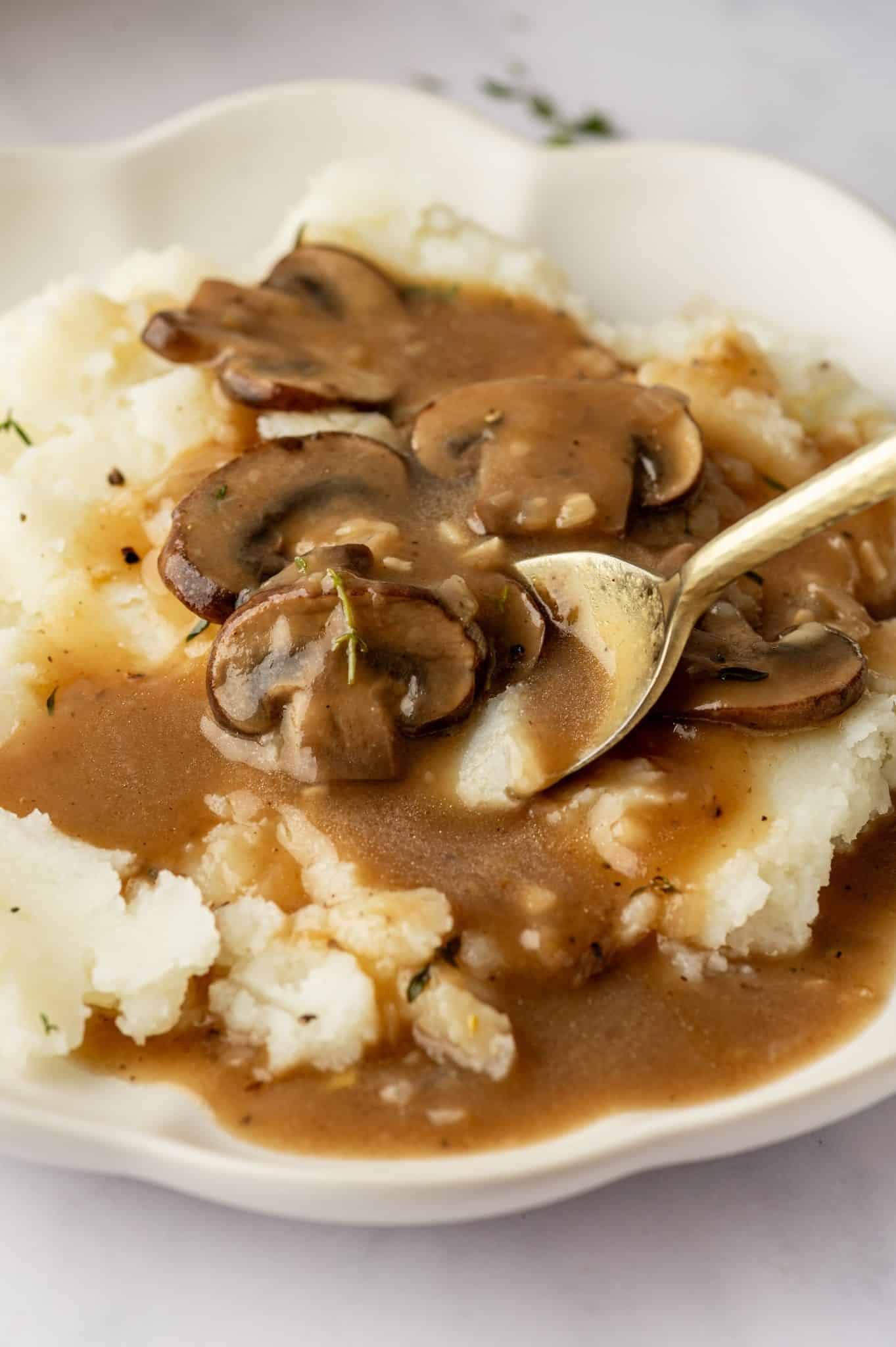Close-up of mushroom gravy over mashed potatoes with a spoon.