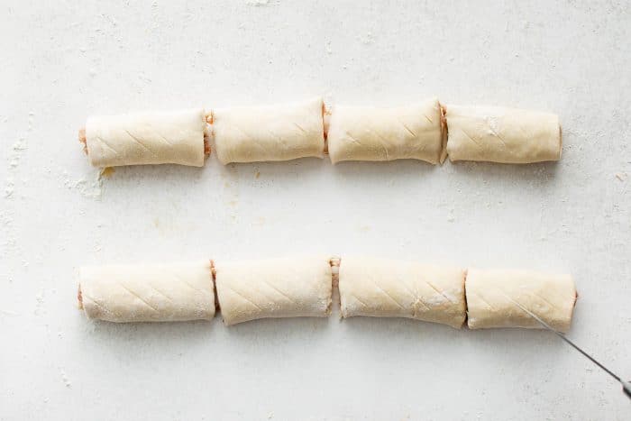Sausage roll logs sliced into pieces with diagonal slits scored on top.