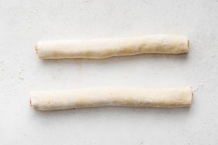 Two long puff pastry logs filled with sausage mixture on a floured surface.
