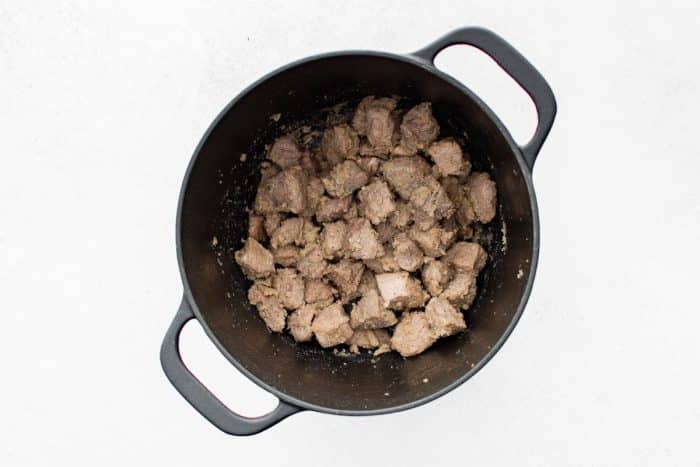 Overhead view of flour-coated pork stew meat in a black Dutch oven, with the flour absorbed and clinging to the pork pieces and a few browned bits stuck around the inside of the pot.