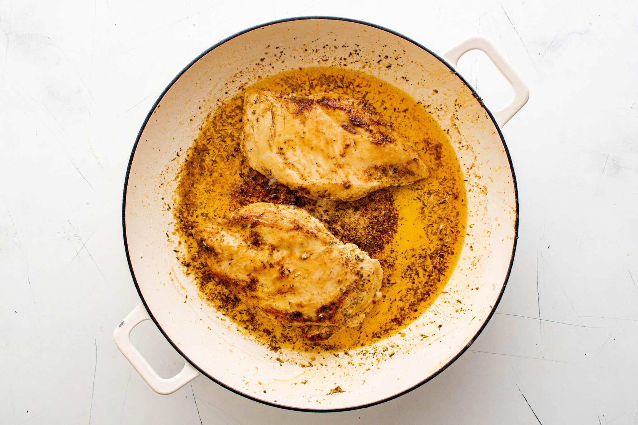 Two well-seasoned and cooked chicken breasts resting in a large skillet.