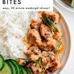 Pinterest pin featuring a close overhead view of a white bowl filled with white rice, Bang Bang salmon bites drizzled with creamy orange sauce, sliced green onions on top, and sliced cucumber rounds on the left side. A second bowl is partially visible at the top right. Bold black text overlay in the upper left reads โBANG BANG SALMON BITESโ and smaller text below reads โeasy, 30 minute weeknight dinner!โ Small gray text near the bottom reads โthe forked spoon.โ