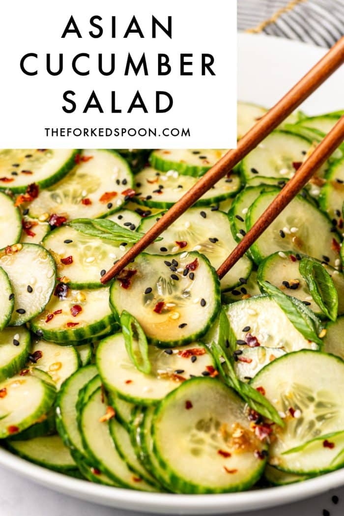 Pinterest pin for Asian cucumber salad showing a close-up of cucumber slices in a large white bowl garnished with sliced green onions, black and white sesame seeds, and red pepper flakes, with wooden chopsticks reaching into the salad. A light gray text box in the upper left corner contains black text that reads “Asian Cucumber Salad” and “theforkedspoon.com.” A gray and white striped towel with gold trim is partially visible in the upper right corner.
