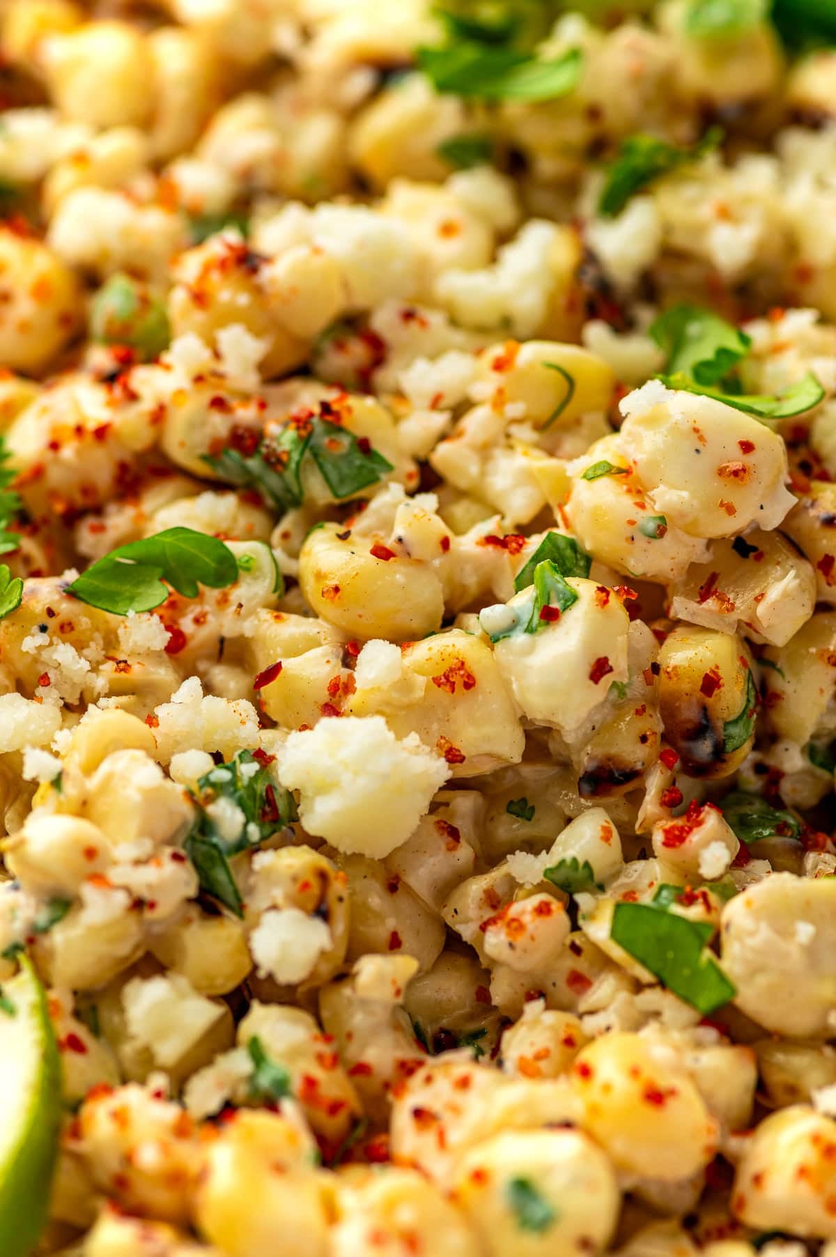 Close-up of creamy Mexican street corn salad with charred corn kernels, crumbled cotija cheese, chopped cilantro, and red chile seasoning.