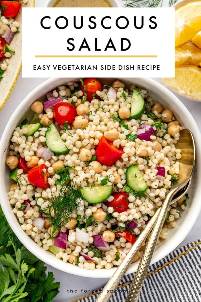 Vertical Pinterest image for couscous salad showing a white bowl filled with pearl couscous salad on a white background. The salad includes chickpeas, halved cherry tomatoes, chopped cucumber, diced red onion, parsley, and dill, with gold serving spoons resting in the bowl. A large white text box overlays the top of the image with black text that reads “COUSCOUS SALAD” and smaller text below that reads “EASY VEGETARIAN SIDE DISH RECIPE,” separated by a thin yellow line. Around the bowl are lemon wedges, a small white bowl of dressing, fresh herbs, part of a serving platter, and a gray and white striped towel with yellow trim. Theforkedspoon.com appears at the bottom.