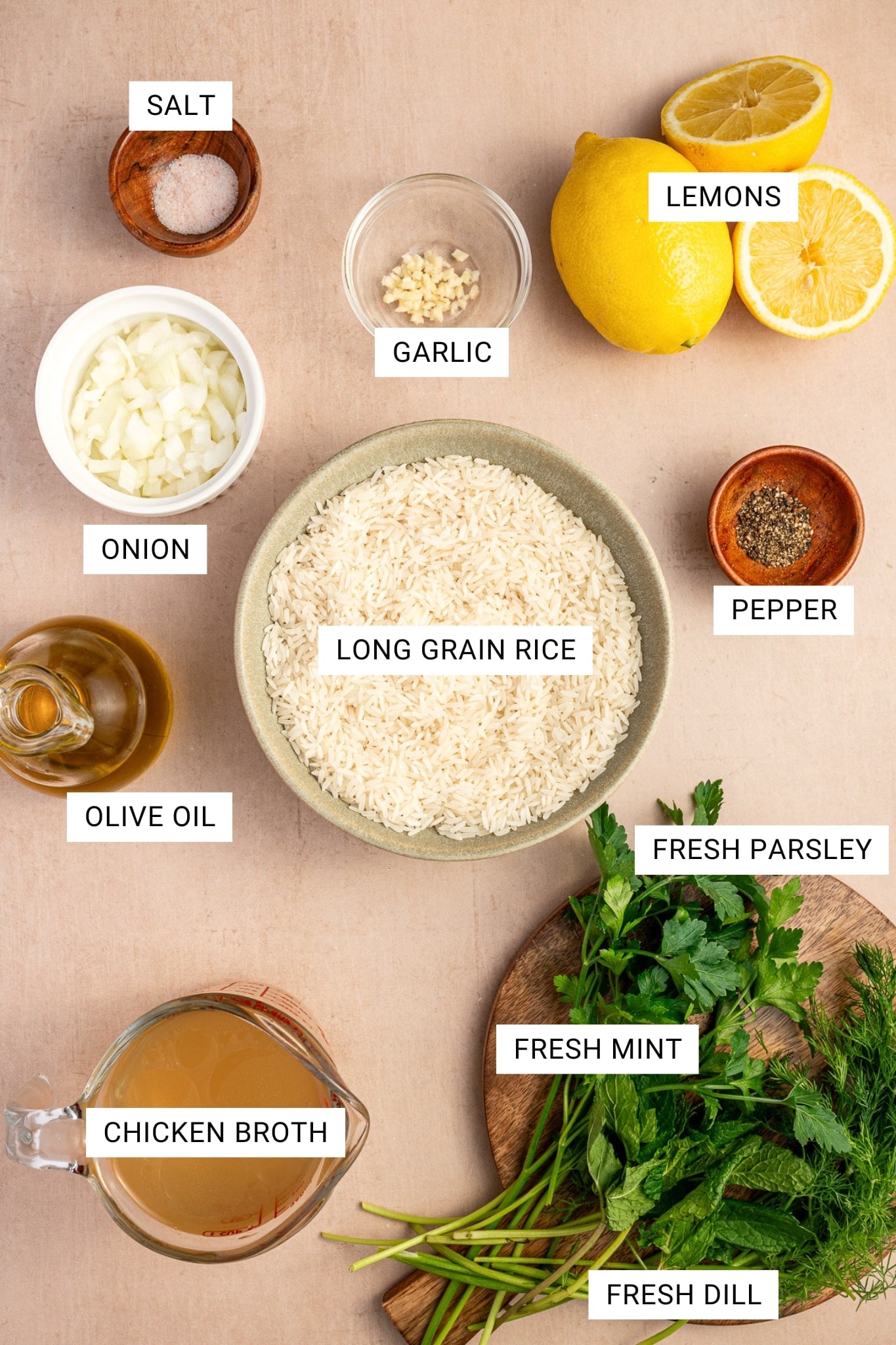 Overhead ingredient image for Greek lemon rice with text labels identifying salt, lemons, garlic, onion, long grain rice, pepper, olive oil, chicken broth, fresh parsley, fresh mint, and fresh dill arranged on a beige surface.