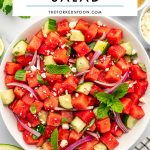 Pinterest pin for watermelon salad showing a large white bowl of cubed watermelon, cucumber, red onion, feta cheese, mint, and basil, with a white text box overlay reading "Watermelon Salad" and "theforkedspoon.com."