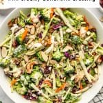 Vertical Pinterest pin showing a bowl of broccoli slaw with broccoli, carrots, red cabbage, cranberries, sliced almonds, and creamy dressing, with a white text box overlay reading "Broccoli Slaw" and "with creamy buttermilk dressing," plus TheForkedSpoon.com at the bottom.