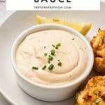 Pinterest image of creamy crab cake sauce in a white ramekin on a white plate with golden crab cakes and lemon wedges, with a white text overlay reading "CRAB CAKE SAUCE" and TheForkedSpoon.com.