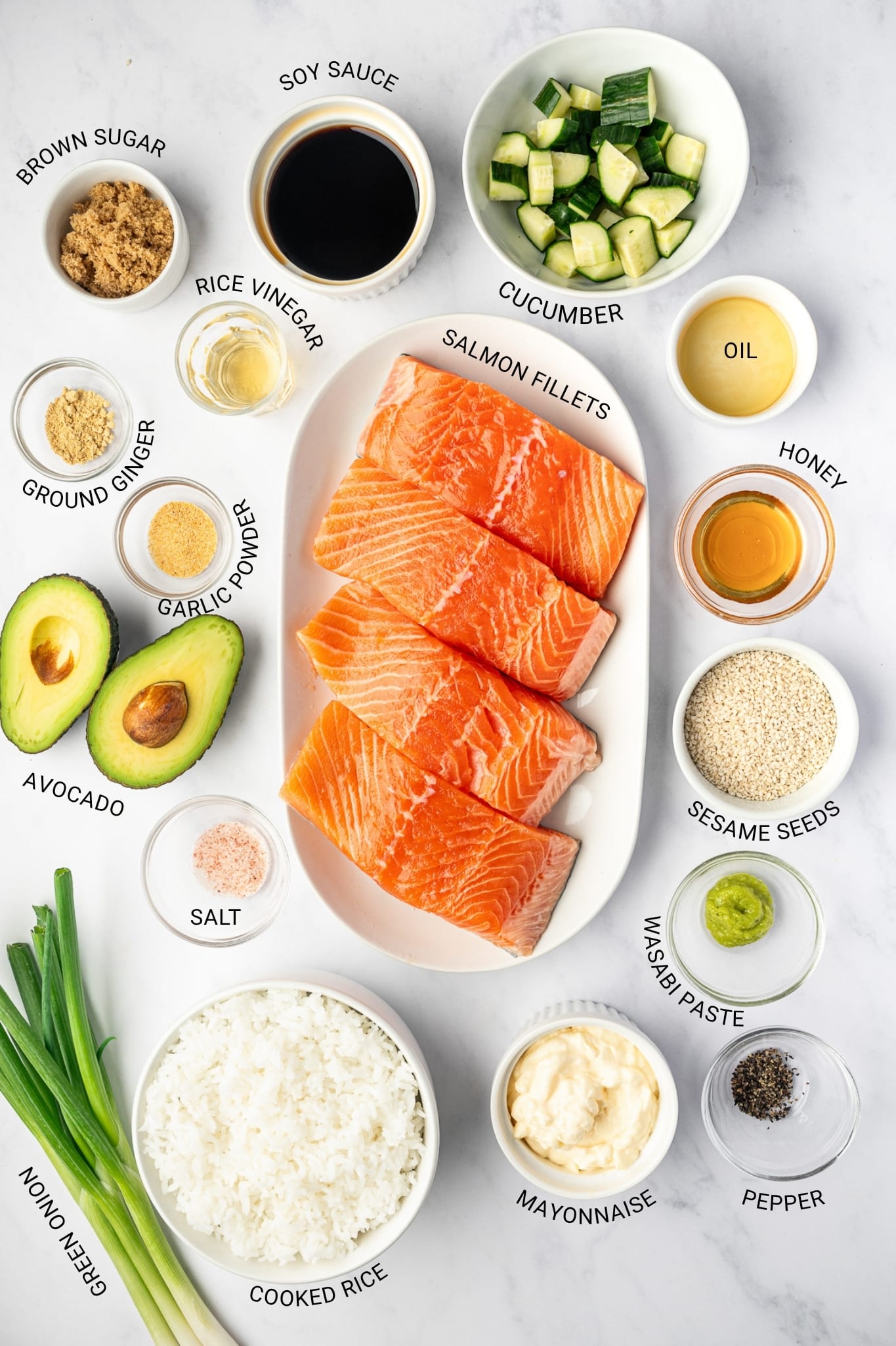 Overhead labeled ingredient image for salmon bowls with raw salmon fillets, cooked rice, avocado, cucumber, green onion, mayonnaise, wasabi paste, soy sauce, honey, oil, rice vinegar, brown sugar, sesame seeds, ginger, garlic powder, salt, and pepper on a white surface.