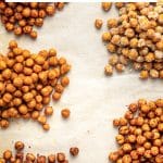 Vertical Pinterest graphic showing five piles of seasoned roasted chickpeas arranged around white parchment paper. A white text box at the top reads "Crispy Roasted Chickpeas" and "Made with canned chickpeas - 6 easy flavors!" with a pink underline and "THEFORKEDSPOON.COM" at the bottom.
