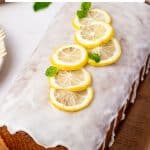 Vertical Pinterest image of a whole golden-brown lemon poppy seed loaf covered with white glaze and topped with thin yellow lemon slices and green mint leaves. A large white banner across the top contains black text reading "Lemon Poppy Seed Bread" and "with simple lemon glaze," while "THEFORKEDSPOON.COM" appears along the bottom.