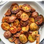 Pinterest graphic featuring a large white bowl filled with crispy roasted red and Yukon Gold baby potatoes garnished with chopped parsley. A white text box at the top reads "Perfectly Crispy Oven-Roasted Potatoes" in black lettering with a yellow underline, and "THEFORKEDSPOON.COM" appears along the bottom.