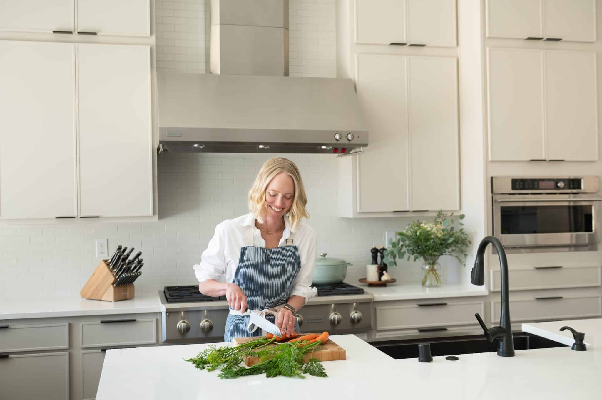 Chef Jessica Randhawa chopping fresh carrots at the kitchen island in her home kitchen.