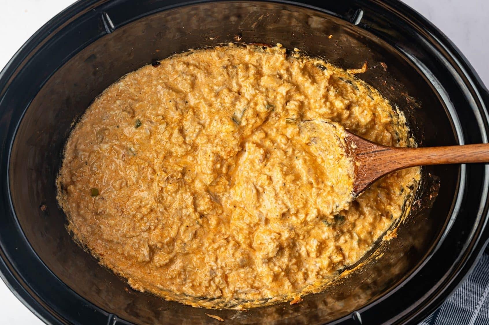 Thick and creamy Buffalo Chicken Dip fully melted and combined inside a slow cooker, with shredded chicken throughout and a wooden spoon resting in the finished dip.