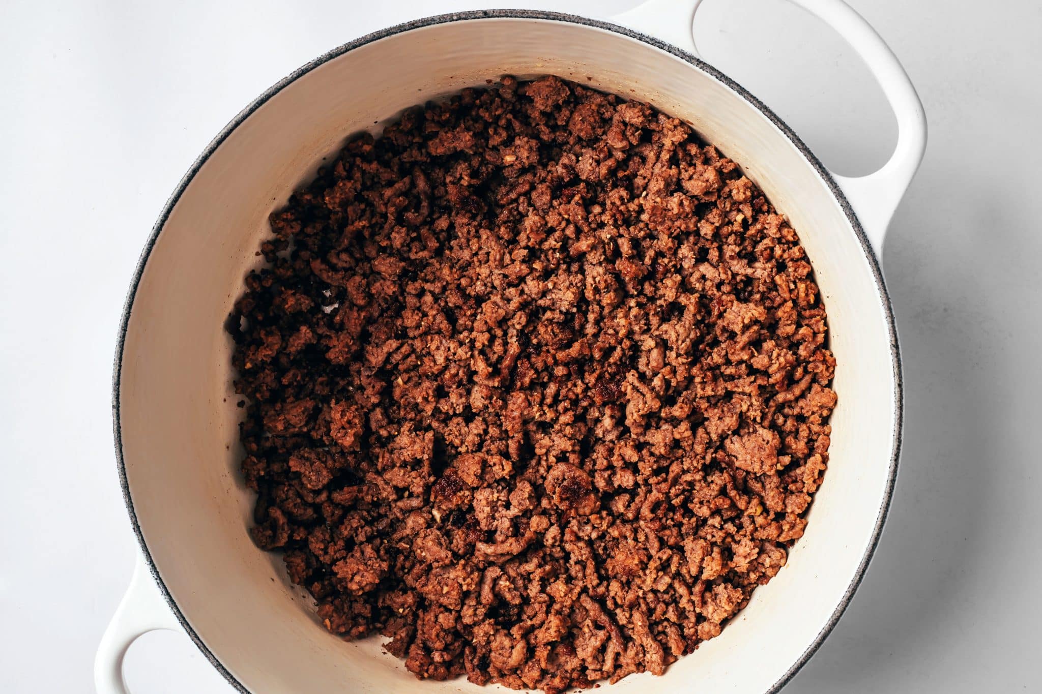Ground beef browned and crumbled in a white Dutch oven until deeply browned, with no visible pink remaining.