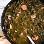 Green gumbo with sausage in pot next to bowl of rice