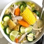 Large white shallow bowl filled with caldo de pollo made with chicken, carrots, corn, lime juice, potatoes, and zucchini.