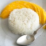 Small serving of mango sticky rice topped with coconut cream and sesame seeds and served with sliced mango.