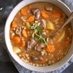 Overhead image of a large soup bowl filled with beef barley soup topped with fresh oregano.