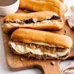 Three warm French dip sandwiches on a cutting board with a bowl of au jus ready to be enjoyed.