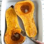 A close up halved roasted butternut squash that has been roasted in a white dish